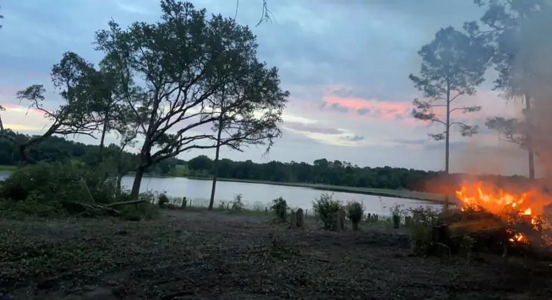 Controlled brush burn glowing at dusk on a cleared Central Florida lot near a lake