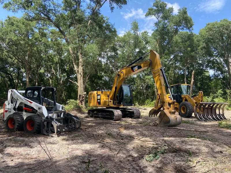 Twisted Pine's own bucket lift, Bobcat skid steer, and CAT excavator lined up on a cleared Central Florida job site
