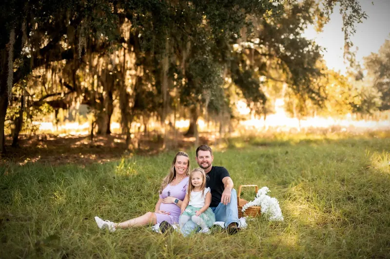 Ryan and his family sitting together in a Florida field under a moss-draped oak tree — the family behind Twisted Pine Tree Service