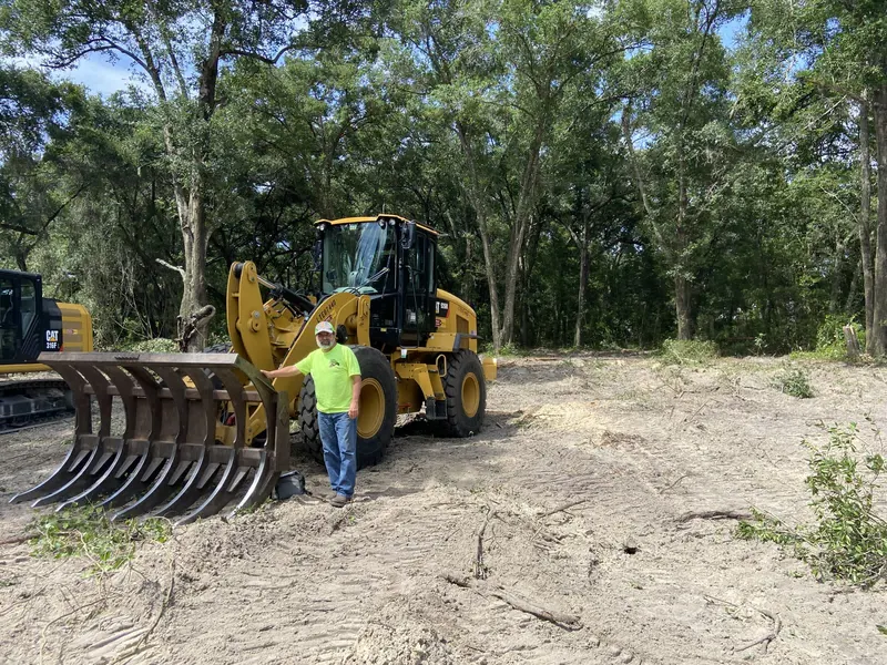 Owner standing beside a CAT wheel loader on a freshly cleared parcel of land, typical of new construction near Wildwood